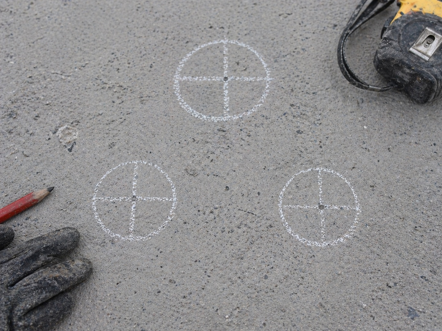 Crosshair set-out marks chalked on a slab next to a tape measure and gloves